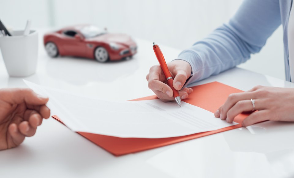 Mujer firma un documento que le ha entrado alguien con una maqueta de un coche al fondo